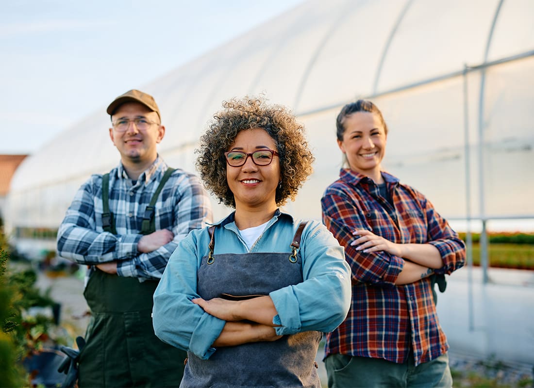 Business Insurance - Group of Three Cheerful Farmers Standing in Front of a Greenhouse on a Sunny Day